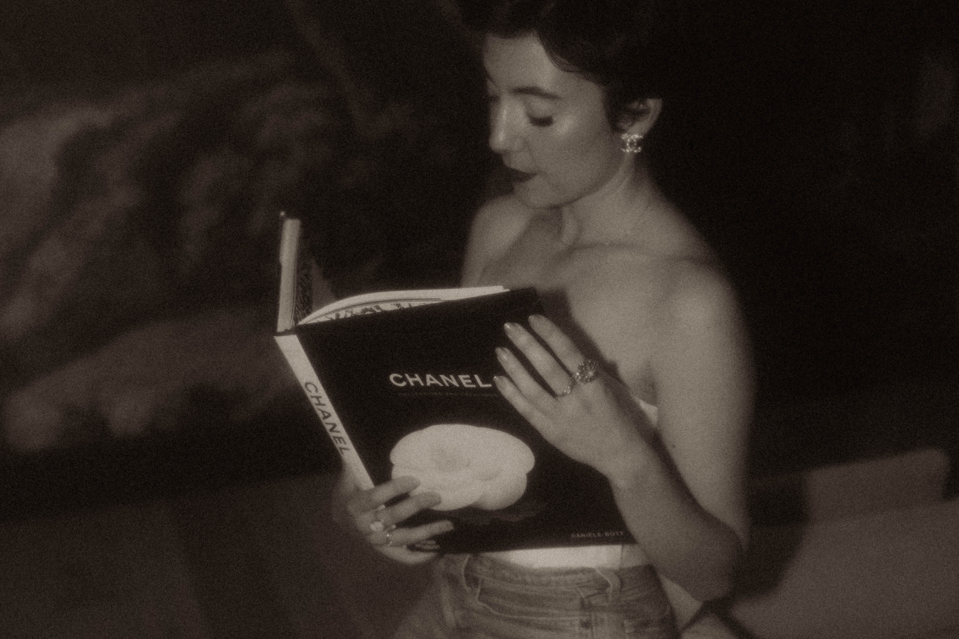 A woman in a strapless top holds a coffee table book of Chanel designs